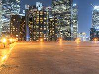 an empty parking lot with skyscrapers in the background at nighttime in an urban area