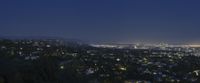 cityscape at night time with a mountain and mountains in the background with trees on either side and small lights in the air