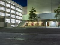 the lights are on in an office building at night time near two trees and a stairway