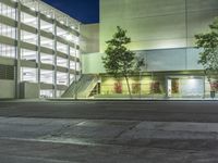 the lights are on in an office building at night time near two trees and a stairway