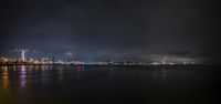 an illuminated city across the water from a beach at night time, illuminated by street lights