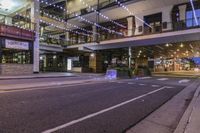 a person is riding down a city street at night with some lights on, and the building is lit up,