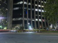 cars driving on a street in front of a large tall building at night time with light streaks