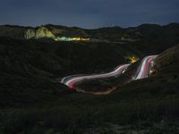 cars are driving down a mountain side road at night, with the lights from cars going on