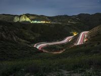 cars are driving down a mountain side road at night, with the lights from cars going on