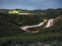 cars are driving down a mountain side road at night, with the lights from cars going on