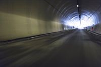 a long tunnel that leads into the distance with people inside and one is driving down the street