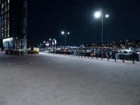 a paved plaza with several lights at night time in front of a city center filled with cars