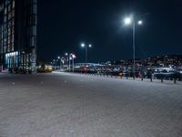 a paved plaza with several lights at night time in front of a city center filled with cars