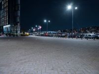 a paved plaza with several lights at night time in front of a city center filled with cars