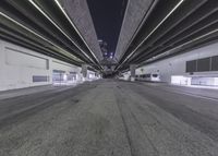 a empty street under a freeway bridge at night time from inside an empty parking garage