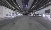 a empty street under a freeway bridge at night time from inside an empty parking garage