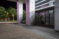 the entrance to a building at night time with the lights on the ground reflecting off of the glass