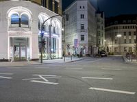 the corner of an intersection on a city street at night with buildings and traffic signs