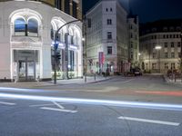 the corner of an intersection on a city street at night with buildings and traffic signs