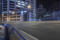 an empty city road at night with skyscrapers in the background in the distance, buildings and street lights visible