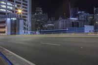 an empty city road at night with skyscrapers in the background in the distance, buildings and street lights visible