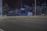 an empty city road at night with skyscrapers in the background in the distance, buildings and street lights visible