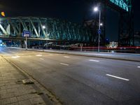 an empty city street near a very tall bridge at night hours time, including driving light trails