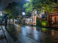 people walking down a street in the rain on a rainy night, with trees behind them