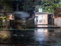 people walking down a street in the rain on a rainy night, with trees behind them