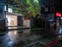 people walking down a street in the rain on a rainy night, with trees behind them