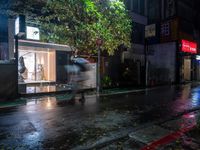 people walking down a street in the rain on a rainy night, with trees behind them