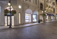 a city street has several shops at night by the sidewalk and light post in front