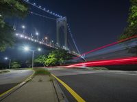 a long shot shows some light streaks on the road below a bridge at night with cars passing by