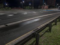 a night time photograph of the empty road with a traffic light on the corner and buildings in the background