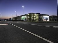 a night time photo of a road and building with lots of lights on it with some people walking along it