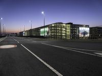 a night time photo of a road and building with lots of lights on it with some people walking along it