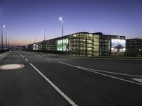 a night time photo of a road and building with lots of lights on it with some people walking along it