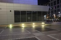 a person riding a skateboard down a paved walkway at night time in front of a large building