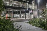 a very large office building surrounded by plants and trees at night time with low lights