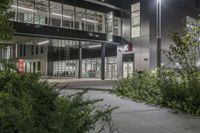 a very large office building surrounded by plants and trees at night time with low lights