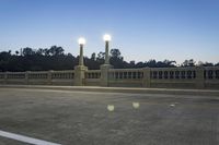 the empty paved bridge has illuminated street lamps lit up at night and people walking over it