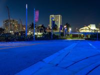 night time street scene, with blue lighting and buildings in the background and some cars driving by