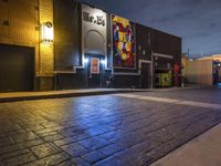a night time street scene with an illuminated store front and people walking on the sidewalk