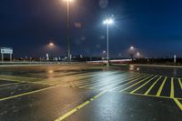 a fork lift is driving through a parking lot at night time with lights on in the background