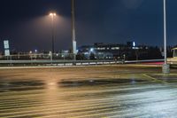 a fork lift is driving through a parking lot at night time with lights on in the background