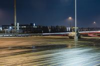 a fork lift is driving through a parking lot at night time with lights on in the background