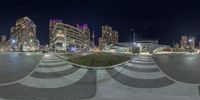 a night time picture of the buildings and street lights in an urban area, with a fish eye lens effect