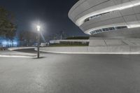 a street lamp stands beside a concrete wall on a city street at night with buildings in the background