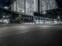 an empty road in front of a building that has some glass on it at night