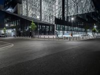 an empty road in front of a building that has some glass on it at night