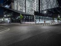 an empty road in front of a building that has some glass on it at night