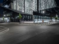 an empty road in front of a building that has some glass on it at night