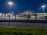 the view from a walkway over a parking lot on a night time, looking at a port container terminal