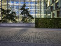 the clock is displayed in front of some tall buildings behind a tree lined street with shrubs